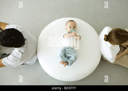 Infant lying on ottoman, mother and father sitting with backs turned, overhead view Stock Photo