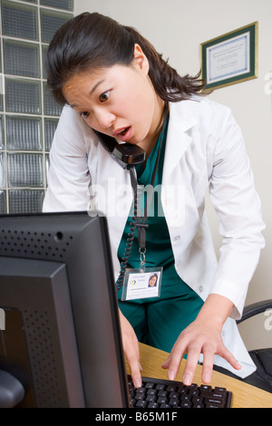 Doctor or nurse looks up patient info on desk top computer. Stock Photo