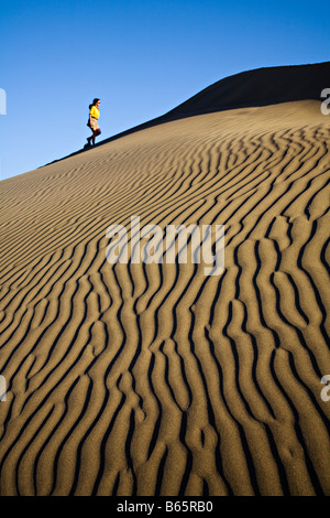 Ripples in sand dune with woman walking up in background Maspalomas Gran Canaria Spain Stock Photo