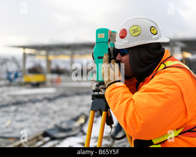 contruction site in winter with surveyor taking a reading on a digital transit theodolite Stock Photo