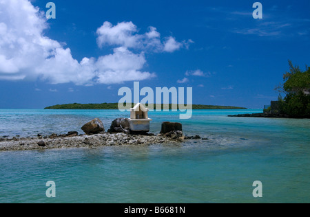 Christian shrine on a rock with turquoise coral filled sea and Ile aux Aigrettes, Mauritius, against a rich blue sky.
