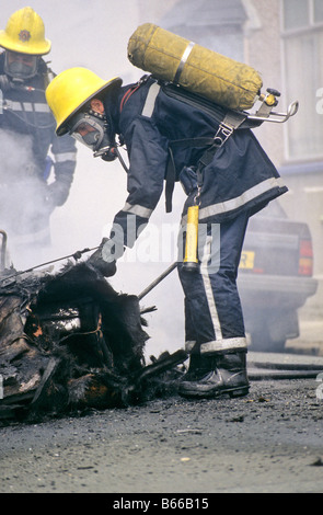 UK British Fireman putting out car fire in street wearing breathing apparatus. Firemen. Devon and Cornwall Fire Brigade Stock Photo