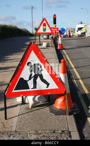 Road works sign with shallow focus and traffic lights in the distance. Stock Photo