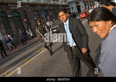 Ecuador Quito Policeman warily watches as man in business suit walks past spectators filling busy city street at Teatro Sucre Stock Photo