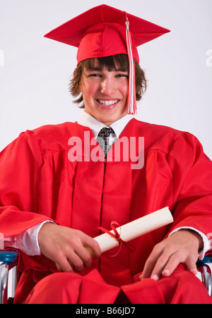 Studio portrait of male graduate in red gown in wheelchair Stock Photo