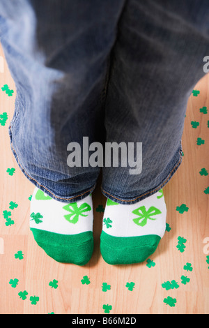 Woman wearing socks with green shamrocks standing on floor amongst shamrocks, low section Stock Photo