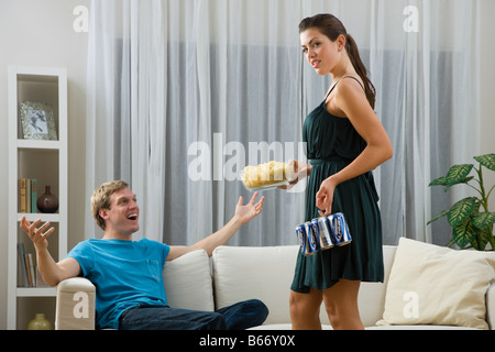 A woman giving a man a bowl of crisps and beer Stock Photo