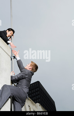 Businessman reaching colleague over wall Stock Photo