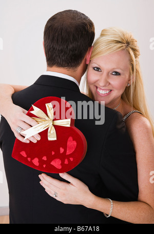 Smiling woman embracing man, holding heart shaped velvet box with ribbon Stock Photo