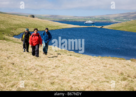 A man and two women walking along the oast, ship in the background, Island of Mousa, Shetland Islands, Scottland, Great Britain Stock Photo