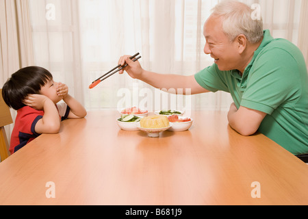 Side profile of a mature man trying to feed a tomato slice to his grandson Stock Photo