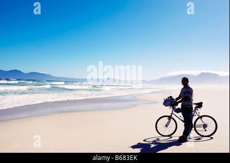 Black man with bike standing on beach Stock Photo