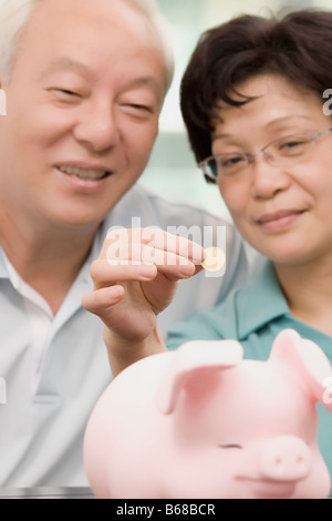 A smiling mature female putting a coin into a piggy bank isolated on ...