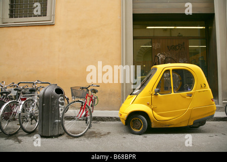 Bicycles and small yellow one-person electric Pasquali Riscio car parked in sidestreet, Florence, Italy. Stock Photo