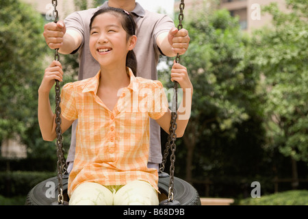 Girl swinging on a tire swing with her father standing behind her Stock Photo