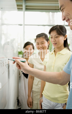 Close-up of a male office worker writing on a whiteboard and three female office workers looking on it Stock Photo