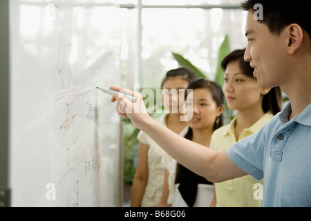 Male office worker writing on a whiteboard and three female office workers looking on it Stock Photo