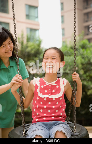Girl swinging on a tire swing with her mother standing behind her Stock Photo