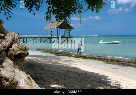 Lazy Sunday, anglers fishing in the Indian Ocean from white coral sand beach and wooden pier, turquoise sea, blue sky and boat. Stock Photo