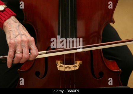 Elderly woman cellist strumming cello strings with bow Stock Photo