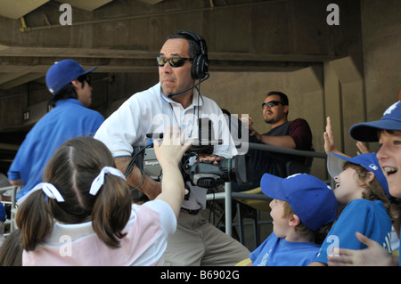 Video camera crew checks big screen while transmitting images of excited young baseball fans Stock Photo