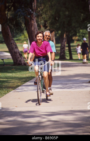 Hispanic couple ride tandem bike in park. Stock Photo