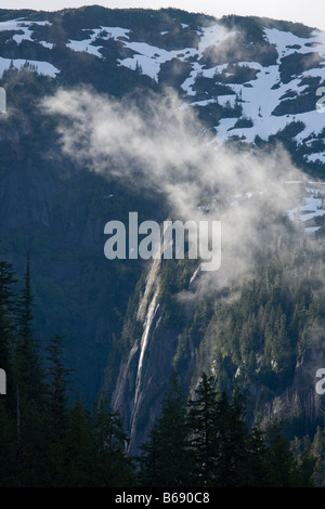 USA Alaska Misty Fjords National Monument Setting sun lights mist rising above rainforest and rocky cliffs above Rudyerd Bay Stock Photo