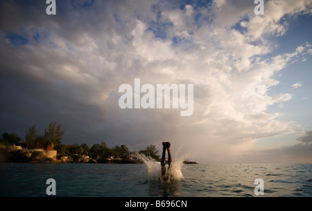 Jamaica Negril Silhouette of young man leaping from from cliff above Pirates Cave Stock Photo