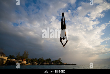 Jamaica Negril Silhouette of young man leaping from from cliff above Pirates Cave Stock Photo