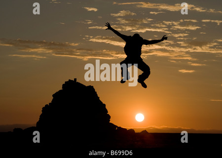 Africa Namibia Namib Naukluft National Park Silhouette of man leaping from rock cairn in desert at sunset Stock Photo