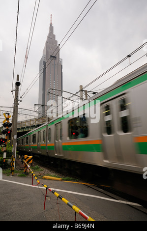 NTT DoCoMo Yoyogi Building (background) and a train in movement on a road through railroad crossing. Shinjuku. Tokyo. Japan. Stock Photo
