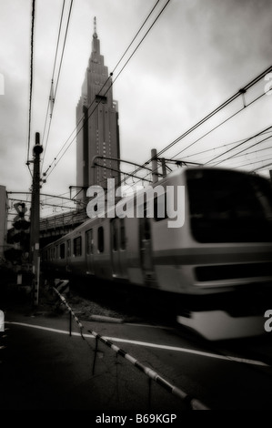 NTT DoCoMo Yoyogi Building (background) and a train in movement on a road through railroad crossing. Shinjuku. Tokyo. Japan. Stock Photo