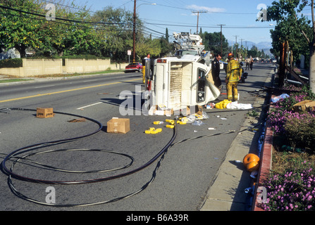 Rescue workers pull driver from overturned truck with wires on road. Stock Photo