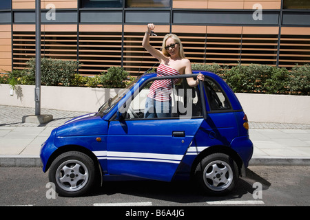 Young woman waving by electric car Stock Photo