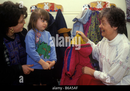 mother saying goodbye to her daughter in the cloakroom of a primary school with a teacher taking her coat Stock Photo