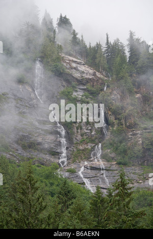 USA Alaska Misty Fjords National Monument Waterfall and rainforest on steep cliffs along Rudyerd Bay on foggy morning Stock Photo