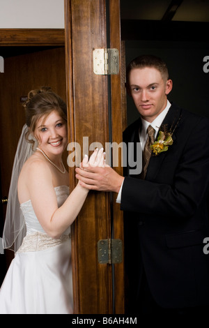 Bride and groom looking at camera from opposite sides of door Stock Photo