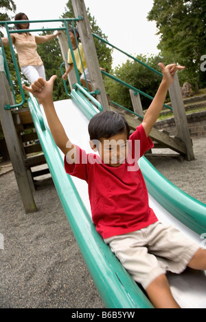 Asian boy sliding down slide on playground Stock Photo