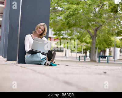 Businesswoman sitting at roadside and using laptop Stock Photo