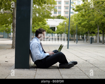 Side profile of businessman sitting at roadside and using laptop Stock Photo