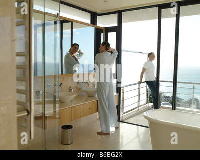 Side profile of woman adjusting her hair at bathroom sink with her husband standing in background Stock Photo