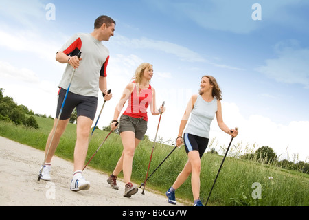 Two women and man walking with hiking poles on dirt road Stock Photo