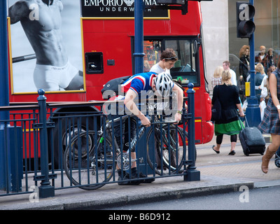 Cyclist chaining his bicycle to a fence with a huge lock Oxford Circus London city UK Stock Photo