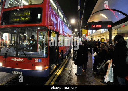 Oxford street bus stop and West End Christmas shopper passengers waiting to board 390 bus & others waiting with electronic timetable London England UK Stock Photo