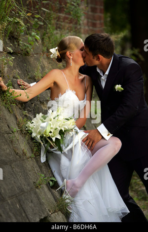 Kissing newlywed couple leaning against wall in countryside Stock Photo