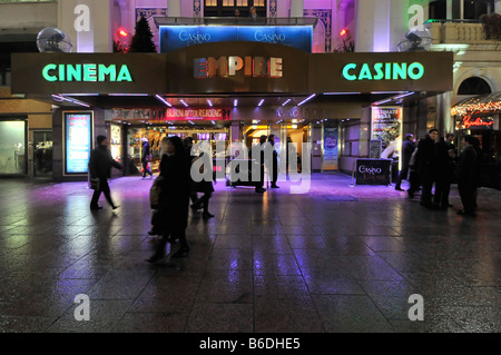 Evening view people on pavement outside Empire Leicester Square cinema casino entertainment premises cerise coloured flood lighting London England UK Stock Photo