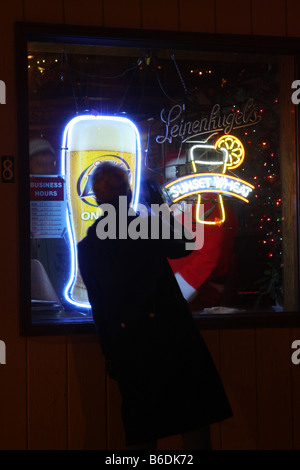 A woman waving to Santa Claus sitting in the window of a bar in Wisconsin with Leinenkugels and Miller Lite Beer signs Stock Photo