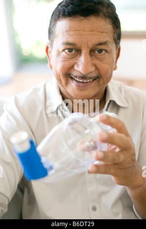 Asthma spacer use. Man using an asthma spacer with a blue asthma inhaler. Stock Photo