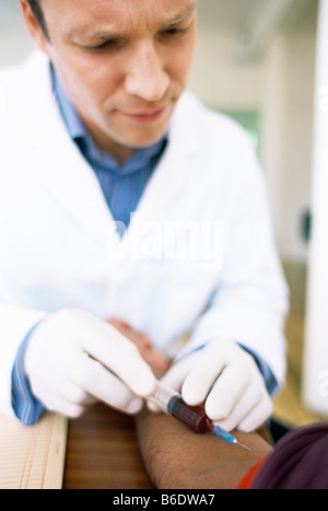 Taking blood. Doctor taking a blood sample from a patient. The red tourniquet around the patient's arm restricts blood flow. Stock Photo