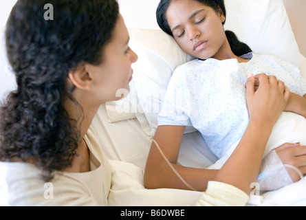 Hospital visit. Mother holding her daughter's hand as she sleeps in a hospital bed. Stock Photo